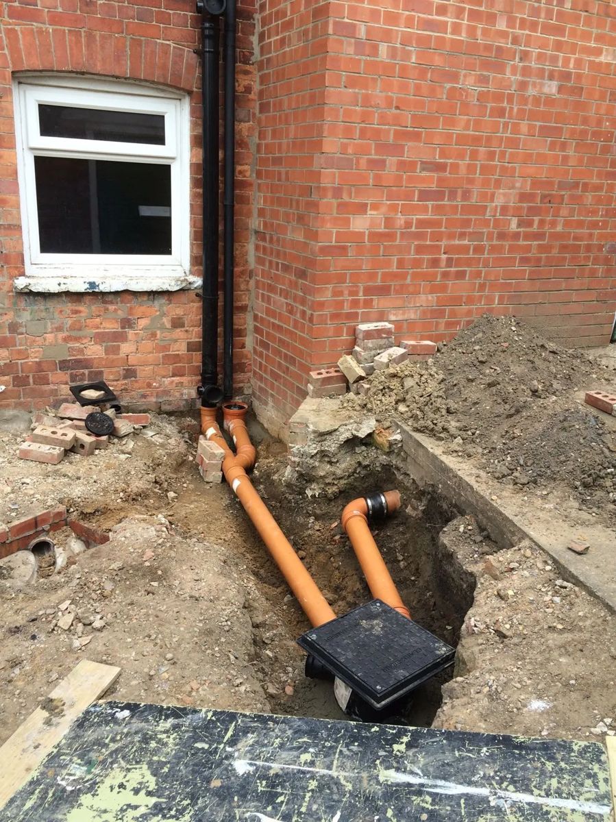 Drain pipes running to an inspection chamber beside a brick wall